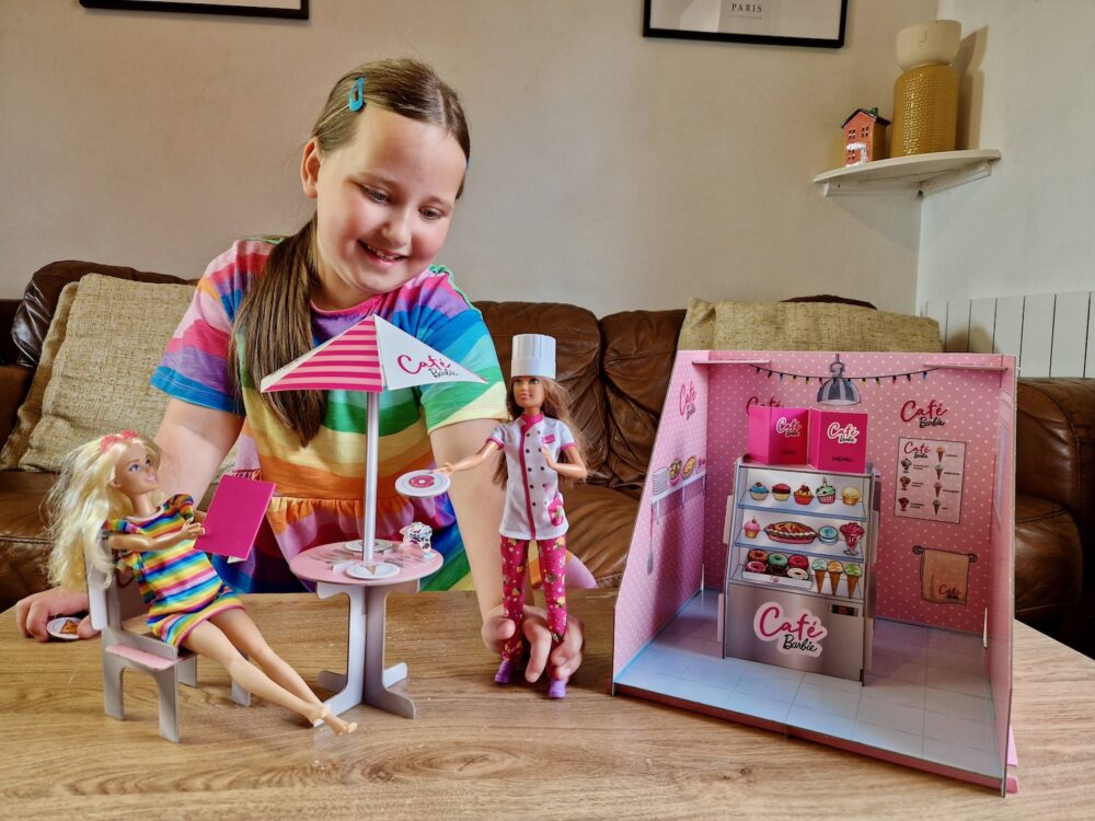 7 year old girl, wearing colourful rainbow dress, playing with the Barbie Pop-Up Cafe, with Pastry Chef Barbie and Barbie with Braces