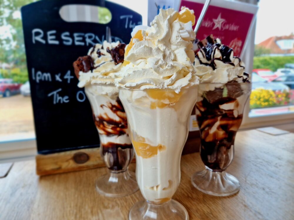 Three ice cream sundaes lined up in front of a menu and reservation board