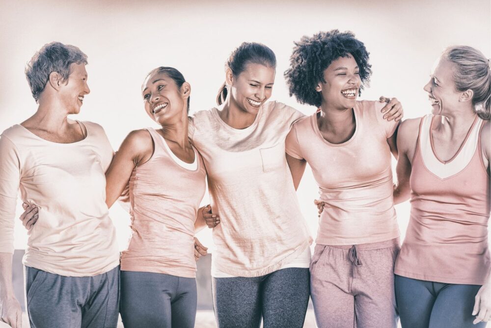 5 women, varying in age, stood in a row. All women are wearing pink tops and jeans