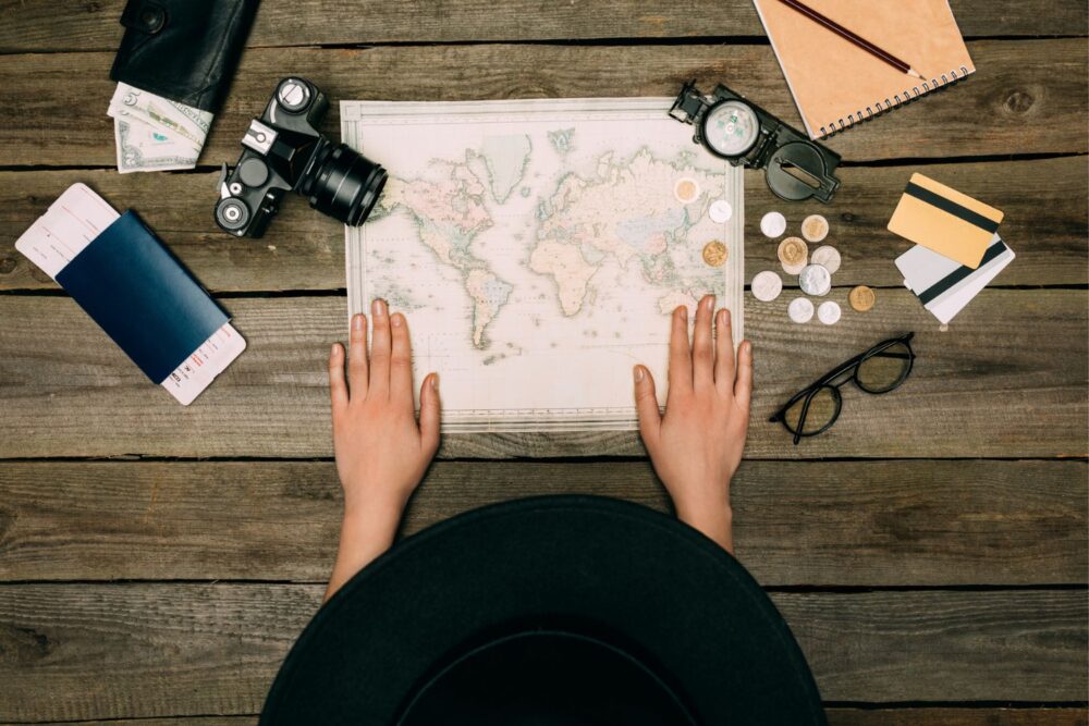Overhead shot of a woman planning her travels, with money, a map and a camera