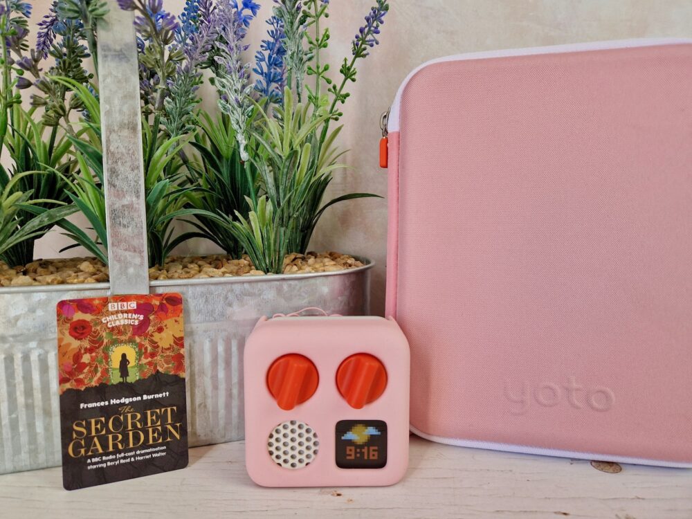 The Secret Garden Yoto Card in front of purple flowers and next to a Yoto Mini player and a card folder