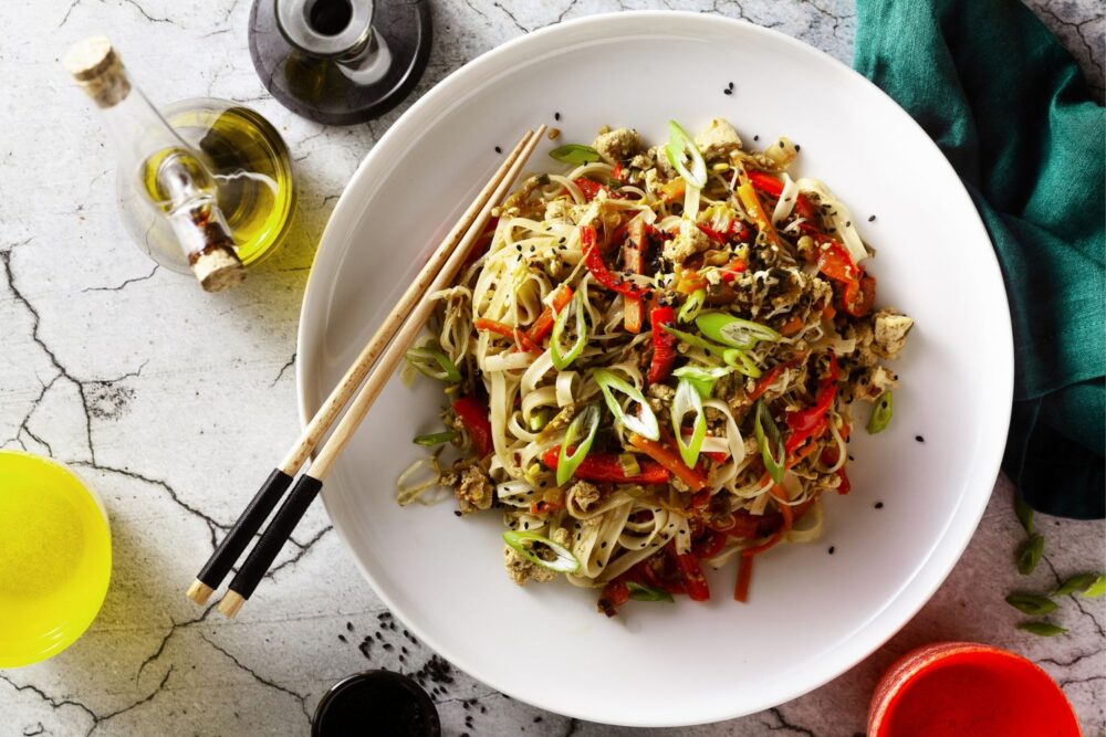 Vegan pad thai rice pasta with vegetables and tofu on gray concrete counter