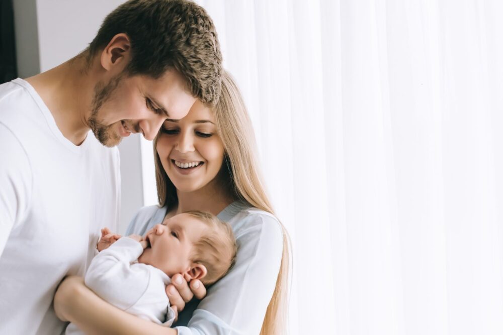 Cheerful family carrying baby boy in front of curtains at home