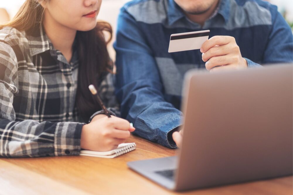 Man and a woman sat in front of a computer, looking at a bank card