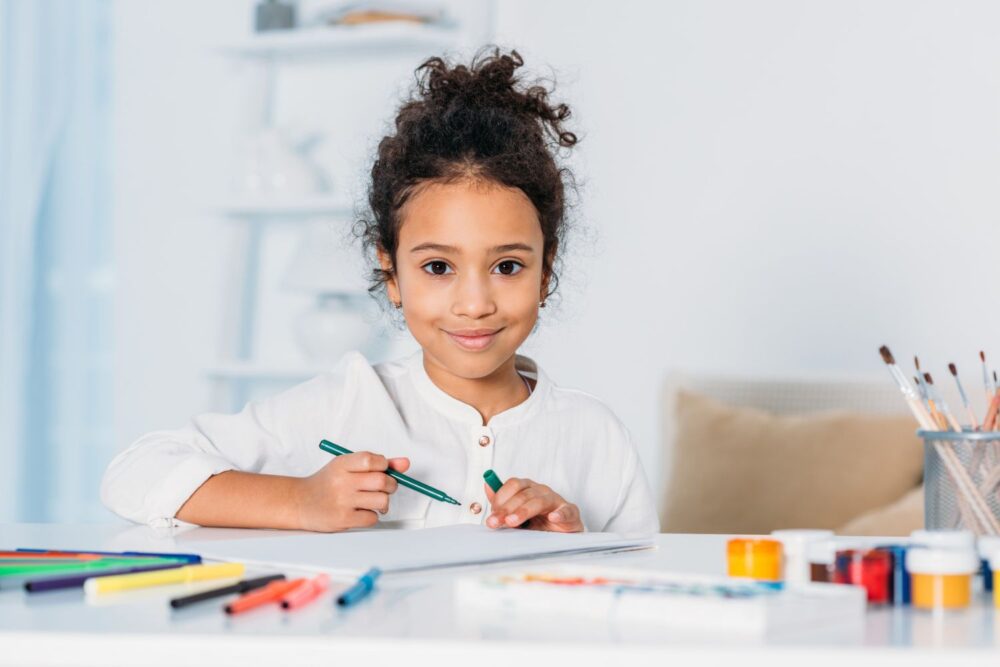 Young child sat at a table, with drawing pens in front of her