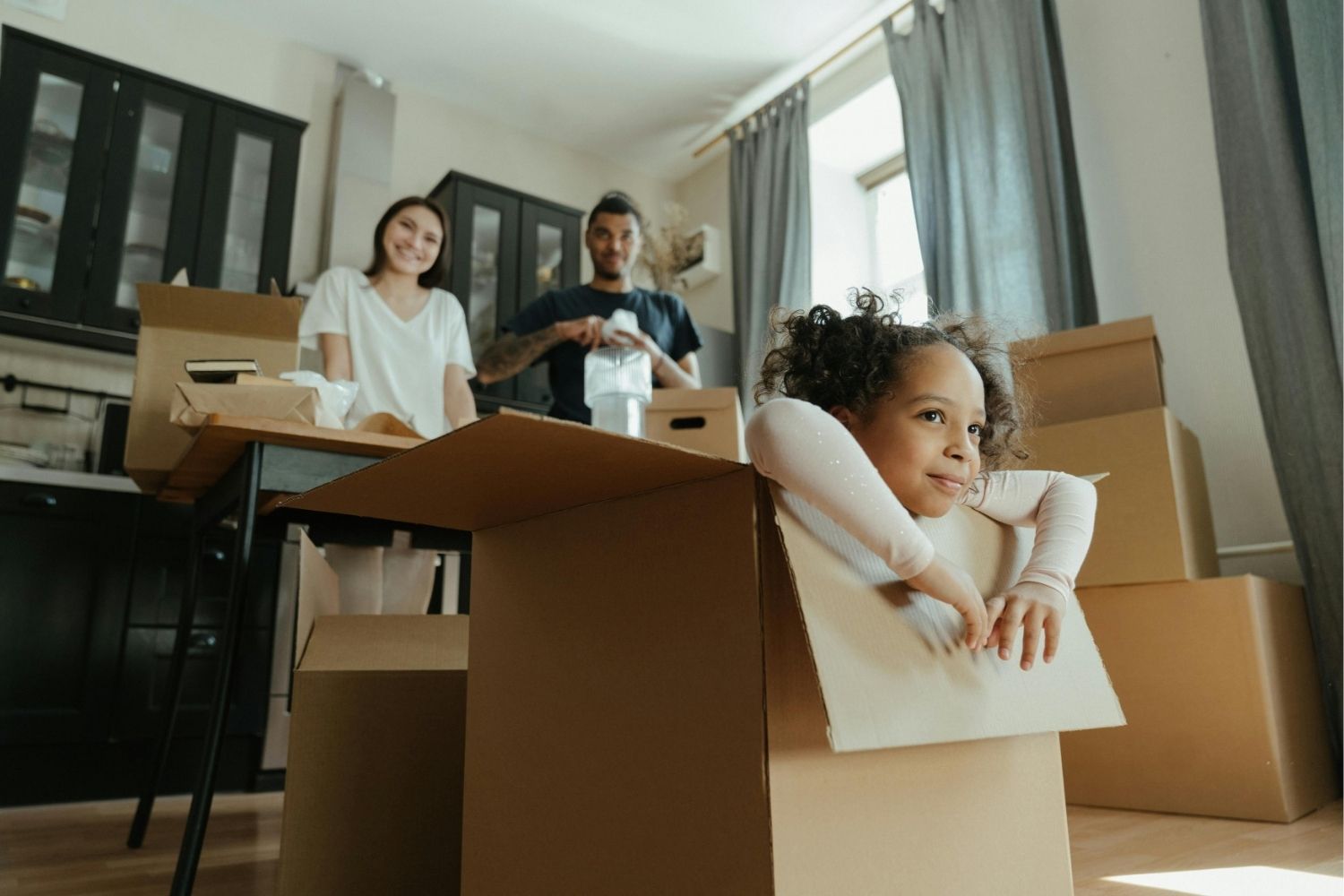 Little Girl Playing in a Box while parents pack up belongings