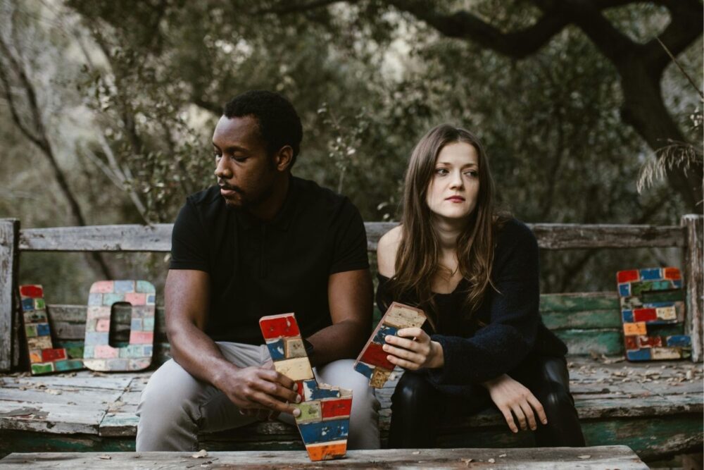 Man and woman sat looking away from each other, holding a broken V