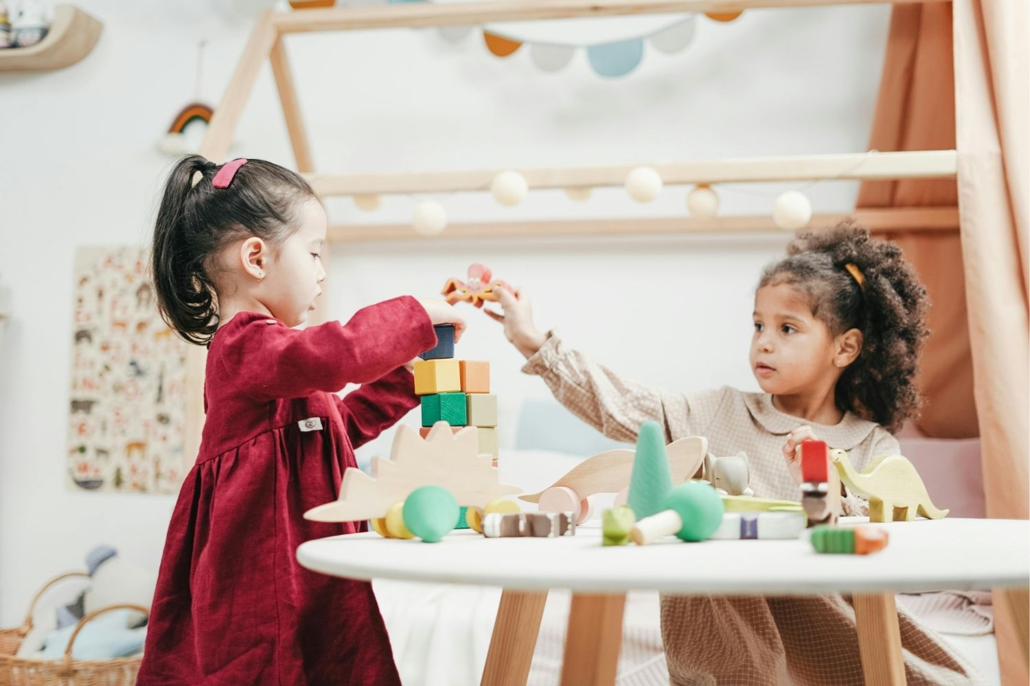 Girl In Red Dress Playing with wooden Blocks with a girl in a tan coloured outfit