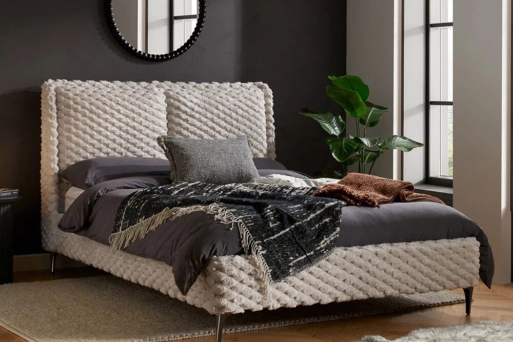 Beige bed with dark bedding against a dark bedroom wall