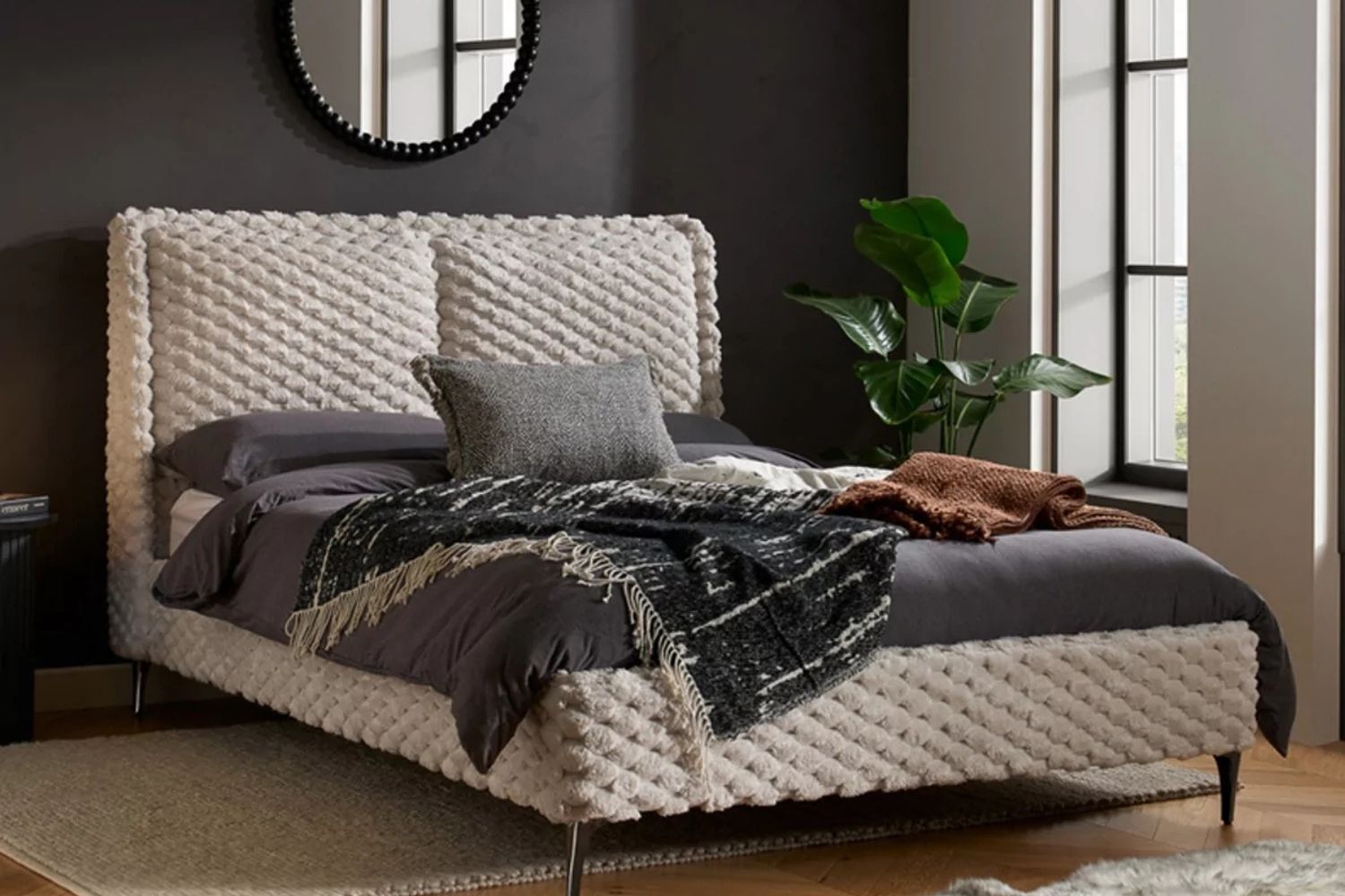 Beige bed with dark bedding against a dark bedroom wall