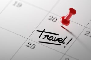 White calendar with red pin in a date that says 'travel'