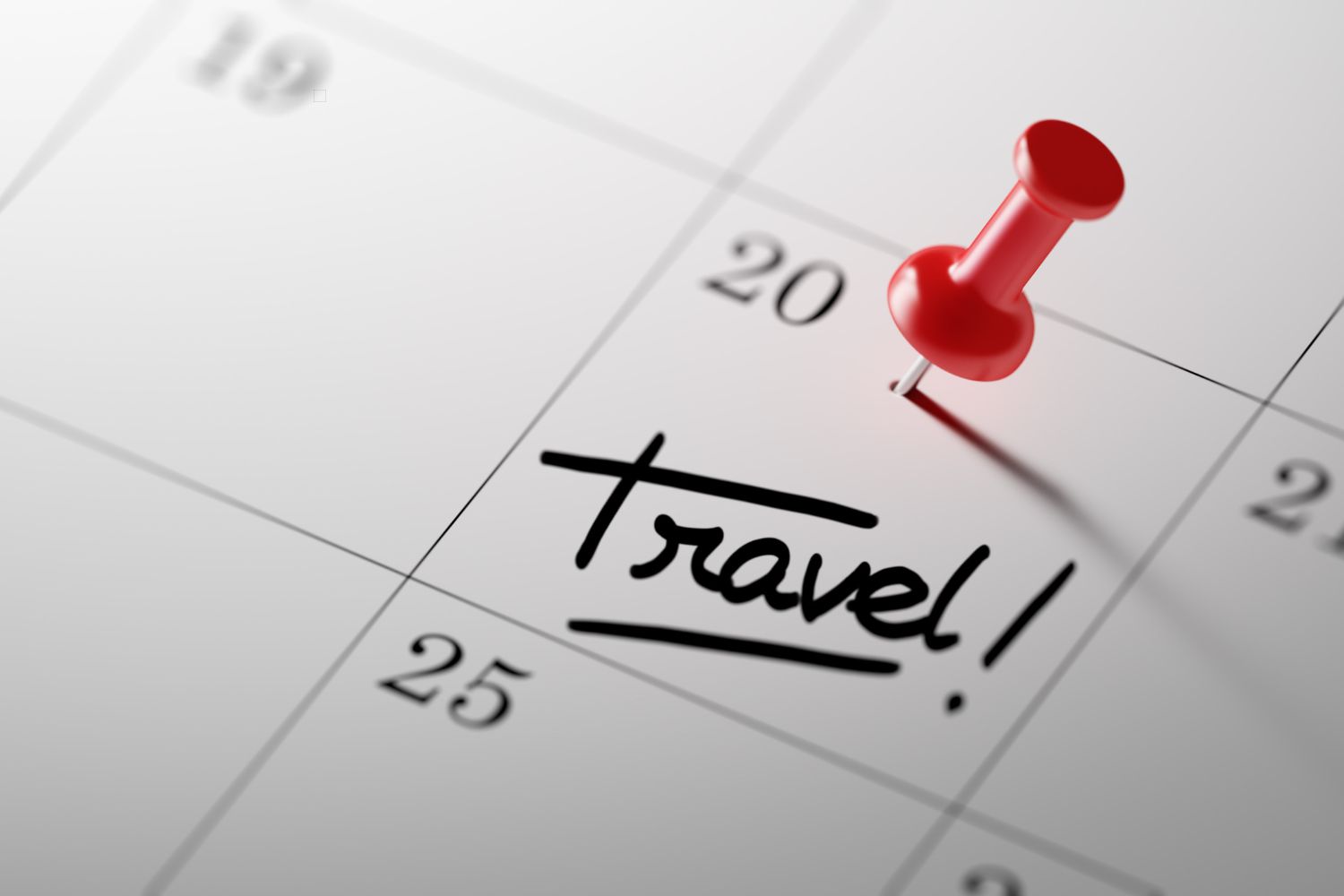 White calendar with red pin in a date that says 'travel'